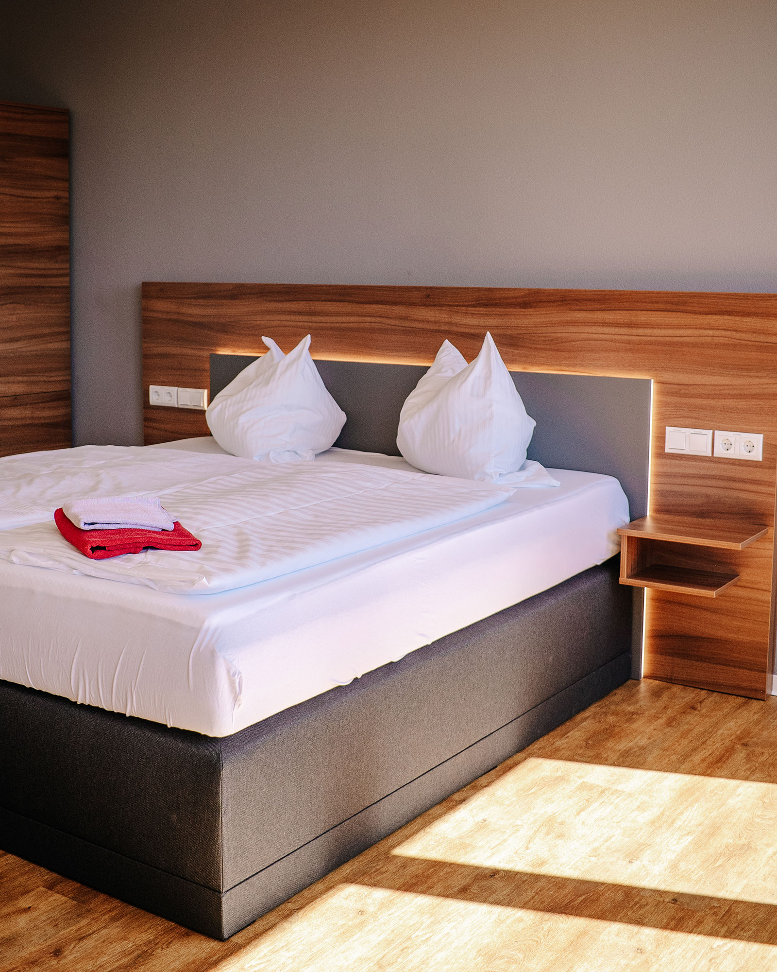 Boxspringbett mit weißer Bettwäsche vor Holzvertäfelung an Wand mit Nachttisch